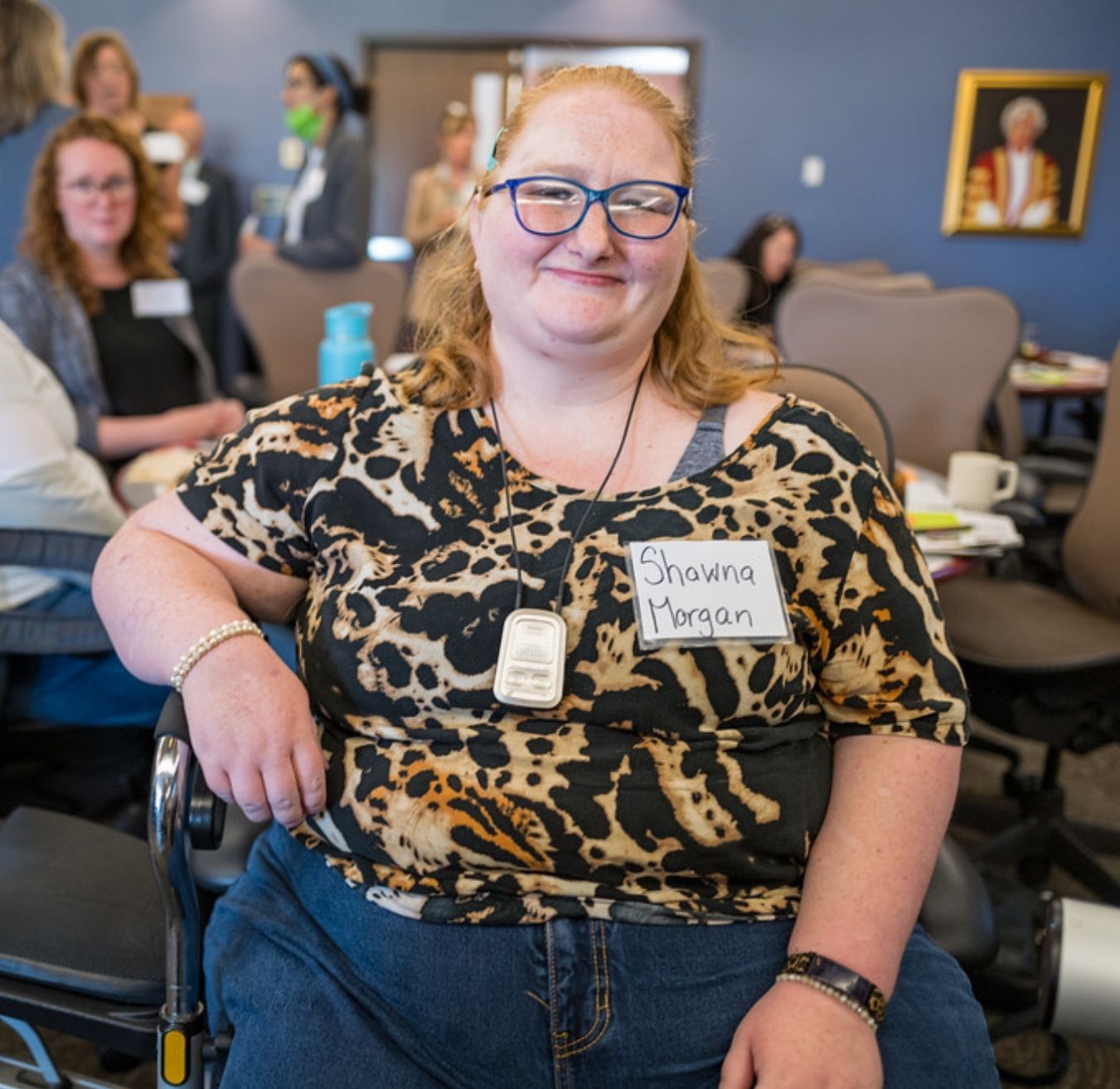 Une femme blanche aux cheveux blonds avec des lunettes, assise et souriante au forum du laboratoire des solutions de logement inclusif au Nouveau-Brunswick.